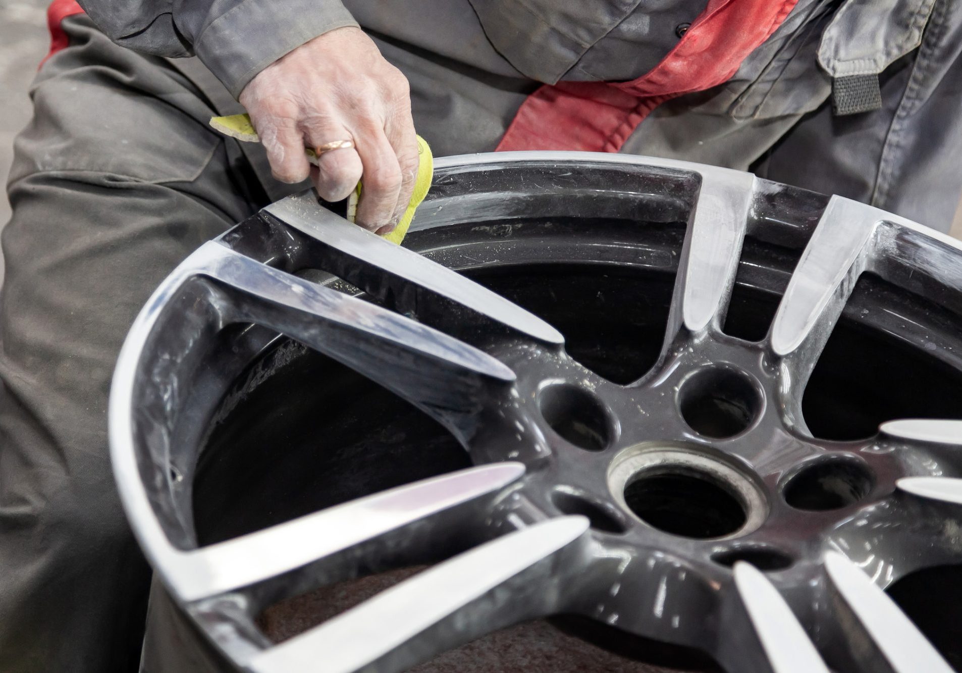 Master body repair man is working on preparing the surface of the aluminum wheel of the car for subsequent painting in the workshop, cleaning and leveling the disk with the help of abrasive material